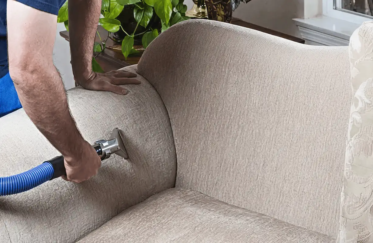 Professional upholstery cleaner deep-cleaning a fabric sofa with a handheld extraction tool and hose, Wilmington, NC.